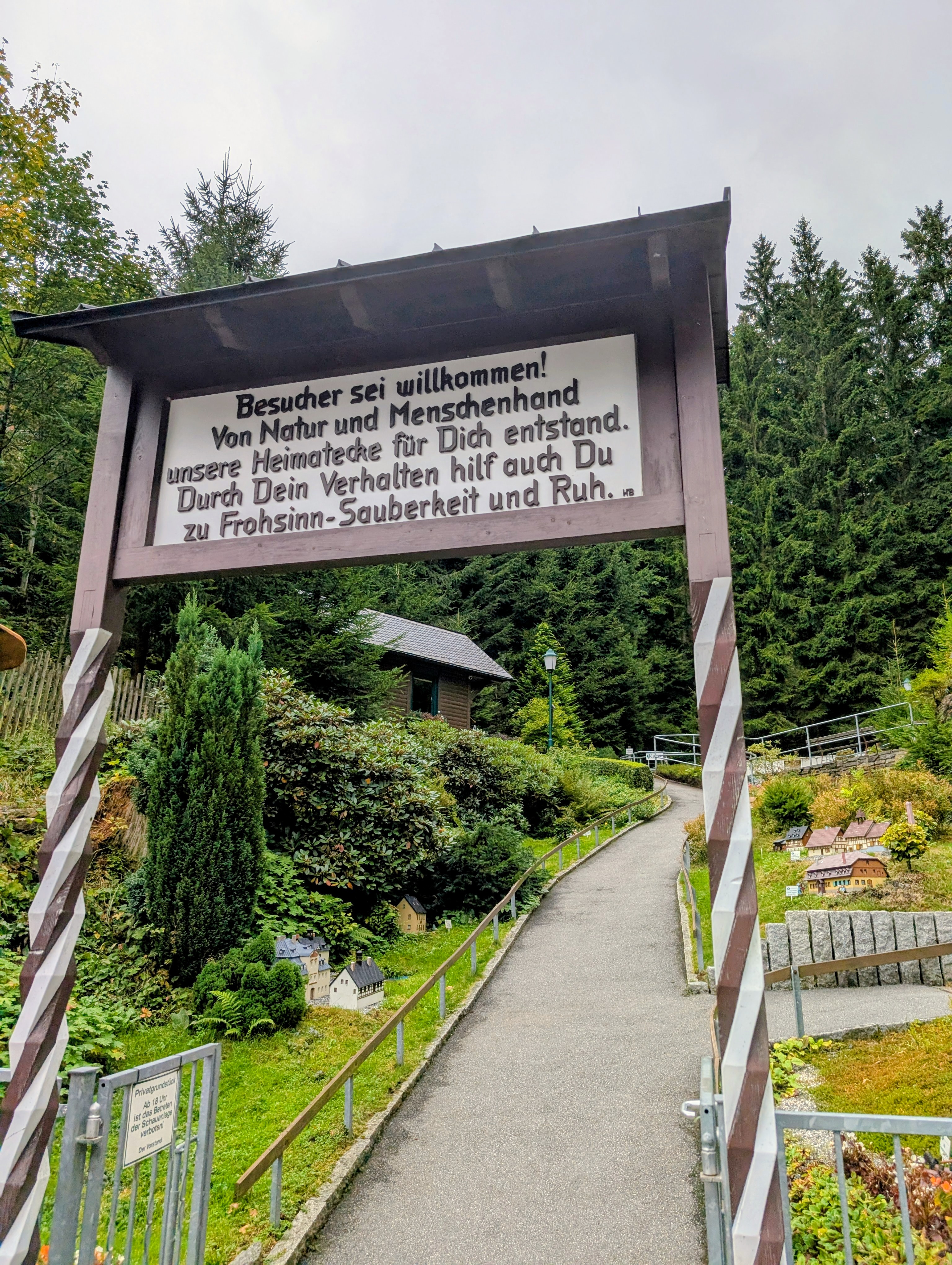 Am Eingang des Museums Heimateck in Waschleithe. Überdachtes Schild, das als Durchgang dient, mit der Aufschrift: "Besucher sei willkommen. Von Natur und Menschenhand unsere Heimatecke für Dich entstand. Durch dein Verhalten hilf auch duzu Frohsinn - Sauberkeit und Ruh."