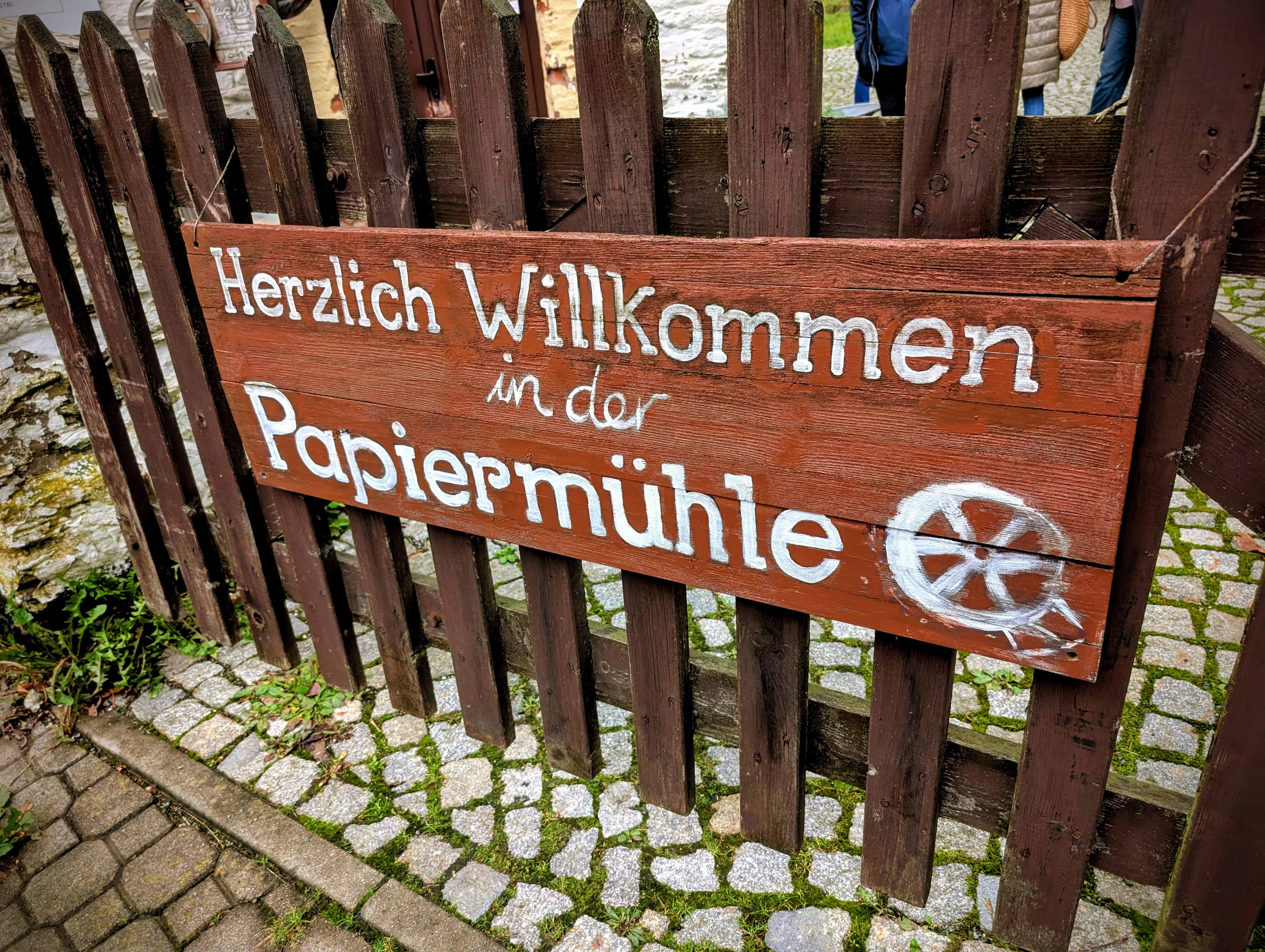 Holzschild an Zaun mit der Aufschrift "Willkommen in der Papiermühle"